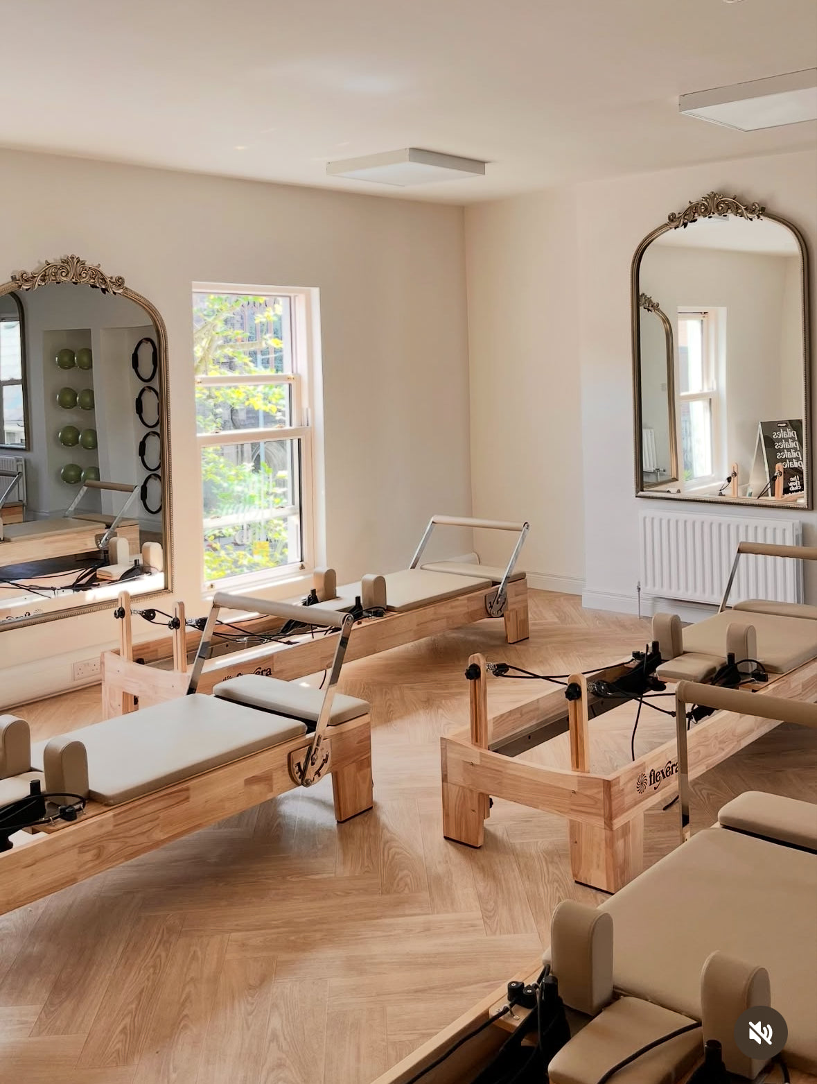 Pilates reformers in a studio with large mirrors and a window.