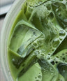 Close-up of iced green tea with ice cubes and foam in a clear cup.