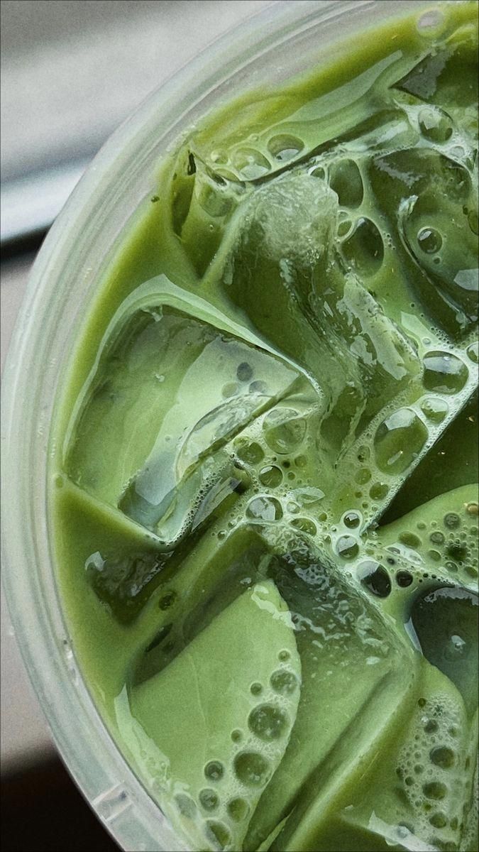 Close-up of iced green tea with ice cubes and foam in a clear cup.